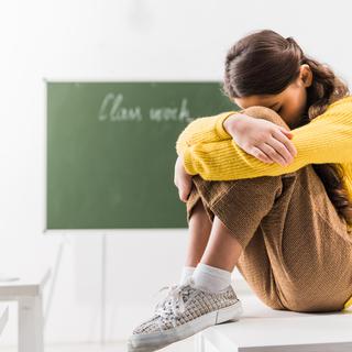 Une jeune fille assise sur son pupitre en classe tient sa tête entre ses genoux. [Depositphotos - VitalikRadko]