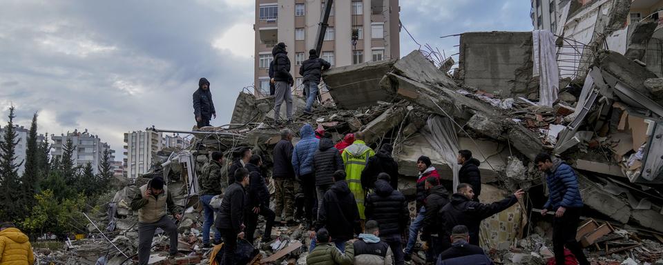 La population turque et les secours recherchent des rescapés dans les décombres d'un bâtiment après le séisme qui a touché le pays. [AP Photo/Keystone - Khalil Hamra]