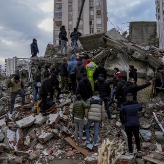 La population turque et les secours recherchent des rescapés dans les décombres d'un bâtiment après le séisme qui a touché le pays. [AP Photo/Keystone - Khalil Hamra]