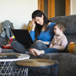 Femme fatiguée travaillant sur un ordinateur portable à la maison avec son enfant. Télétravail de mère célibataire. [Depositphotos - ©Dirima]