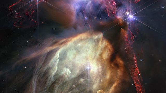 Vu la proximité de Rho Ophiuchi, le JWST a capturé beaucoup de détails de cette formation. Au centre, une cavité géante est creusées grâce à des photons ultraviolets par une seule étoile, S1, plus massive que le Soleil. La couleur jaune-orange provient de minuscules grains de suie appelés hydrocarbures aromatiques polycycliques. La grande bande verticale rouge est un écoulement protostellaire: des jets puissants de matière se produisant aux premiers stades de la formation des étoiles. L'ensemble de la structure rougeoie en raison de l'hydrogène moléculaire énergisé lorsque la matière des jets entre en collision avec le gaz interstellaire. [NASA, ESA, CSA - Greg Bacon (STScI)]