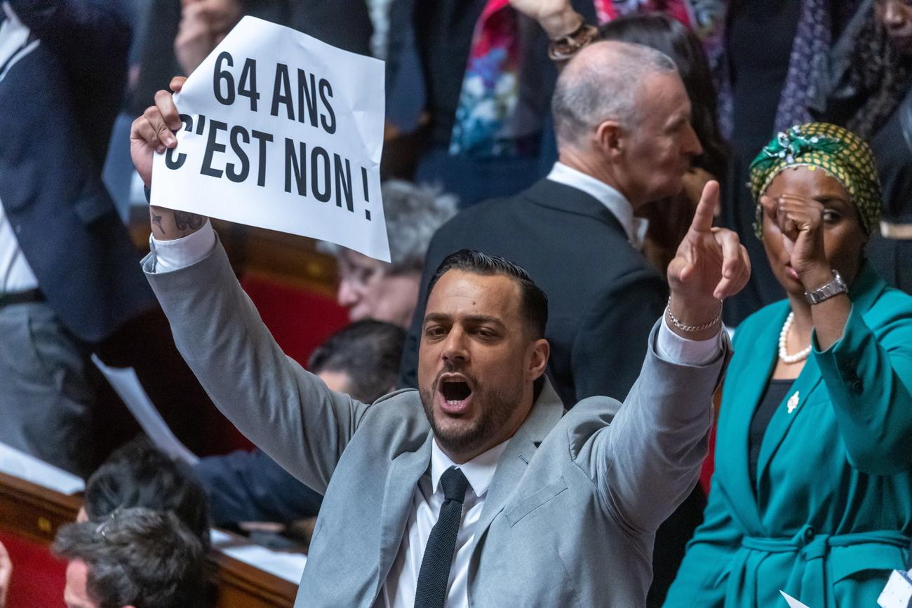 Le député français de la coalition NUPES (Nouvelle Union Écologique et Sociale) Sébastien Delogu montre une affiche sur laquelle on peut lire " Non aux 64 ans " à l'Assemblée nationale à Paris, France, le 16 mars 2023. [Keystone - EPA/CHRISTOPHE PETIT TESSON]