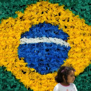 Une petite fille brésilienne en face d'un drapeau de son pays en plastique recyclé (image d'illustration). [Keystone/AP Photo - Eraldo Peres]