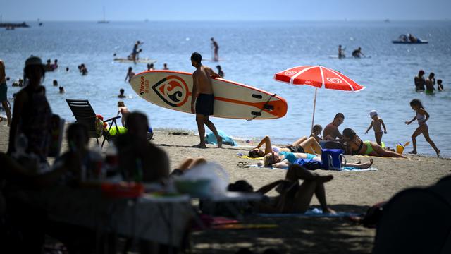 People cooling off in the shade of trees and a person carries his paddle board during warm weather on the shore of the Lake Geneva at the Vidy beach (plage de Vidy) in Lausanne, Switzerland, Sunday, June 19, 2022. People flocked to parks and pools across Western Europe on Sunday for a bit of respite from an early heat wave that saw the mercury rise above 40 Cs (104 F) in France and Spain, and highs of 38 C (100.4 F) in Germany and 36 C in Switzerland. (KEYSTONE/Laurent Gillieron) [Keystone - Laurent Gillieron]
