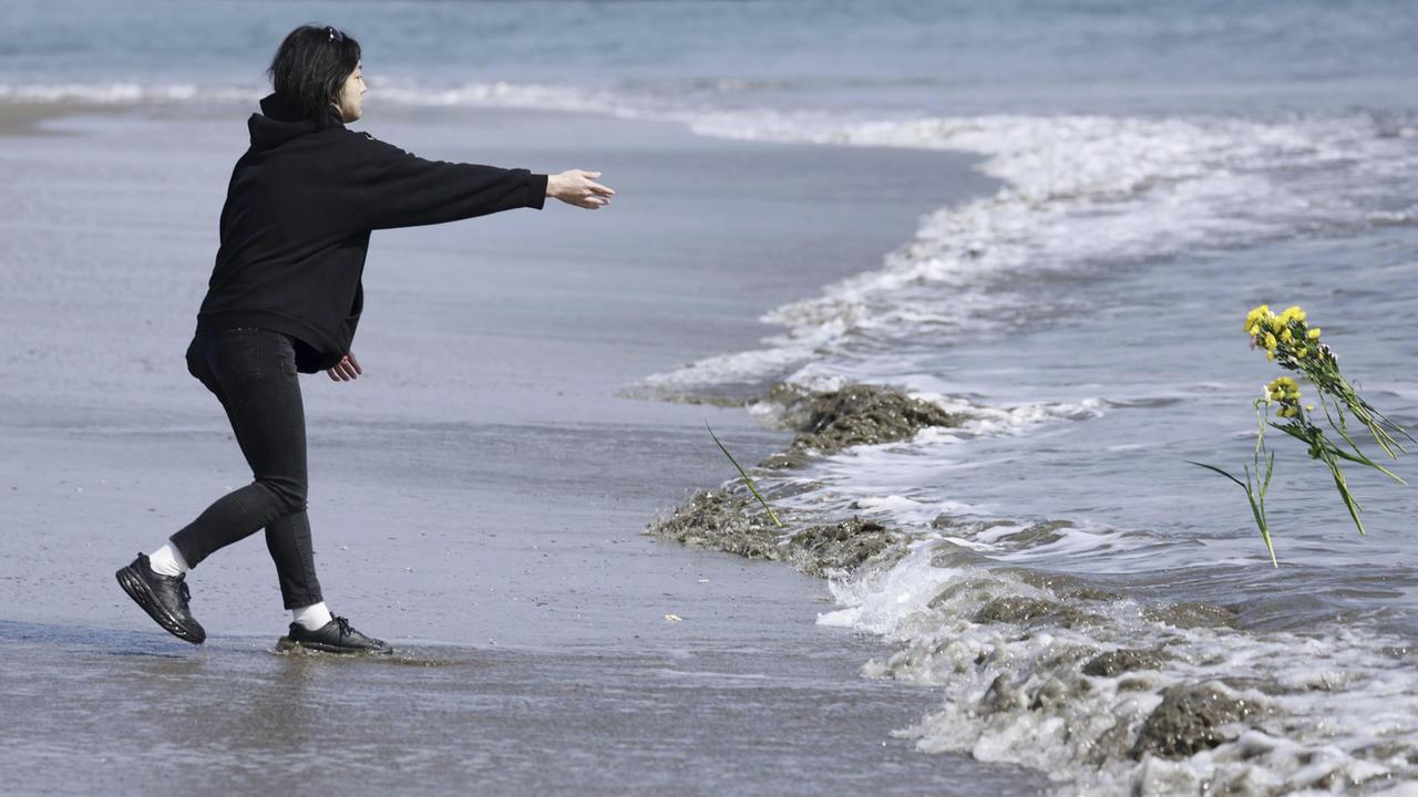 Un homme lance des fleurs à la mer à l'occasion des 12 ans de la catastrophe de Fukushima. [Keystone/AP - Kyodo News]
