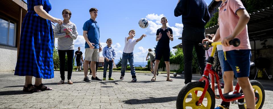 Des enfants et adultes ukrainiens de la region de Marioupol jouent dans la cour d'une maison à Gilly (VD). [Keystone - Jean-Christophe Bott]