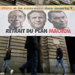 Des passants marchent à proximité d'une bannière de Force ouvrière contestant le projet de réforme des retraites du gouvernement, à Rennes, le 10 janvier 2023. [AFP - DAMIEN MEYER]