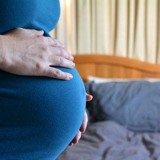 Gros plan sur le ventre d'une femme enceinte avec un lit en arrière-plan. [Depositphotos - lucidwaters]