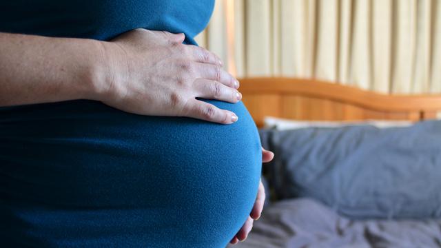 Gros plan sur le ventre d'une femme enceinte avec un lit en arrière-plan. [Depositphotos - lucidwaters]