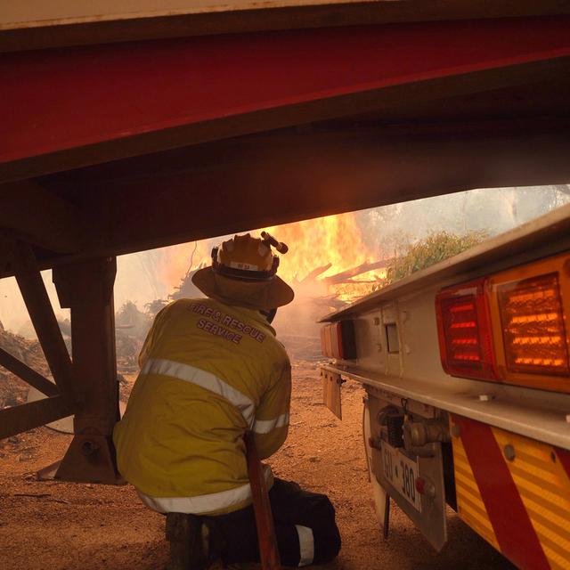 Un pompier s'abrite sous un camion et une remorque alors qu'il travaille sur un incendie près de Wooroloo, au nord-est de Perth, en Australie, le mardi 2 février 2021. [Keystone - EVAN COLLIS]