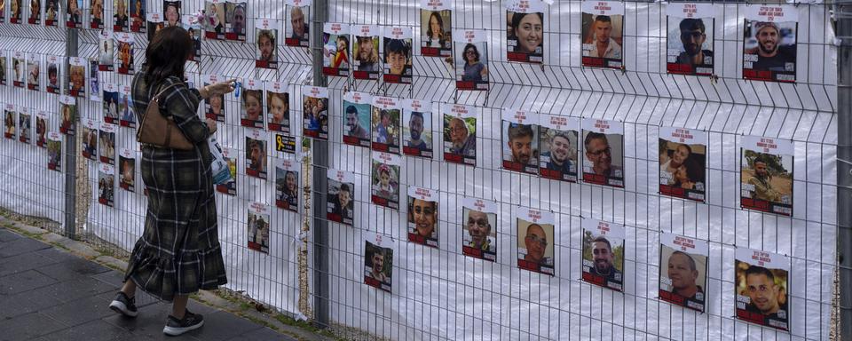 Une femme devant les portraits des otages kidnappés lors de l'attaque du 7 octobre. [Keystone/AP Photo - Oded Balilty]