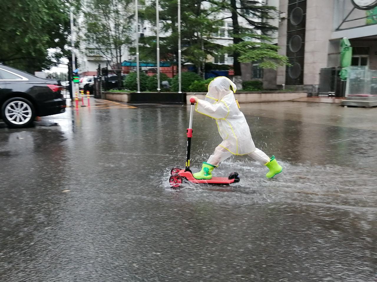 Un enfant joue à la trottinette sous la pluie à Pékin, le 30 juillet 2023. [NURPHOTO VIA AFP - CFOTO]