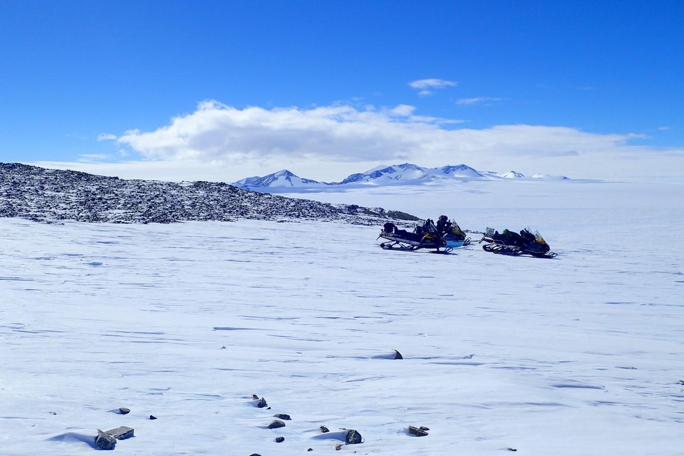 La météorite de 7,6 kilos a été trouvée dans un vaste champ de glace bleue se trouvant entre les motoneiges garées vers une moraine et les montagnes Sør Rondane, au loin. [ETH Zürich - Maria Schönbächler]