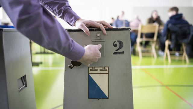 Un volontaire ouvre l'urne pour les élections cantonales de 2023 à Zürich. [Keystone - Ennio Leanza]