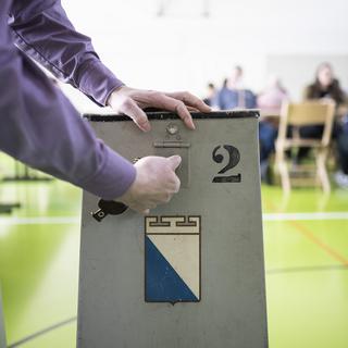 Un volontaire ouvre l'urne pour les élections cantonales de 2023 à Zürich. [Keystone - Ennio Leanza]