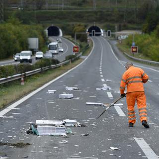 Un employé déblaye les restes d'un véhicule après un accident sur l'autoroute A9. [Keystone - Jean-Christophe Bott]