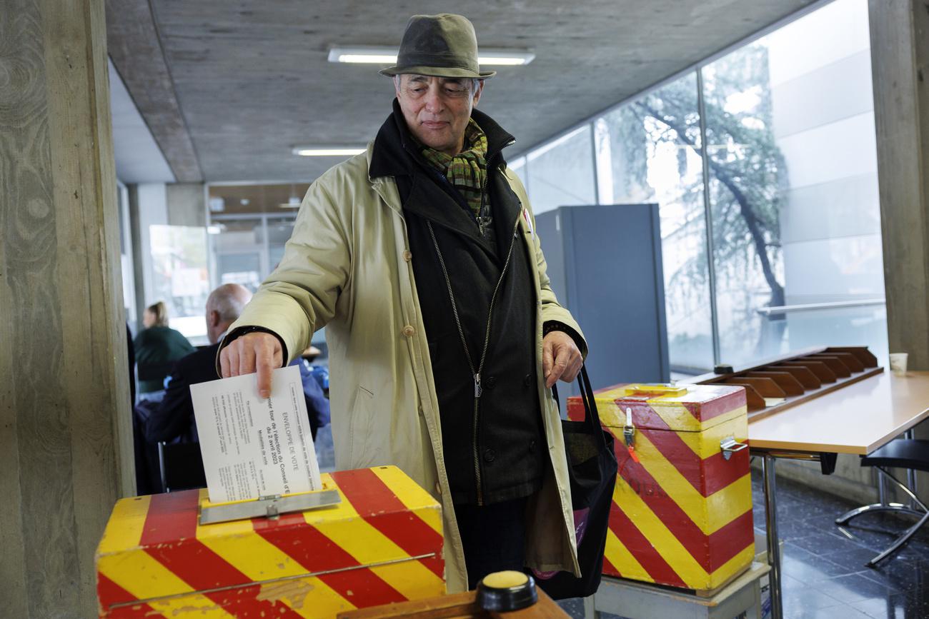 Un citoyen glisse son bulletin de vote dans l'urne aux couleurs genevoises dans le bureau de vote de Carouge (GE). [Keystone - Salvatore Di Nolfi]