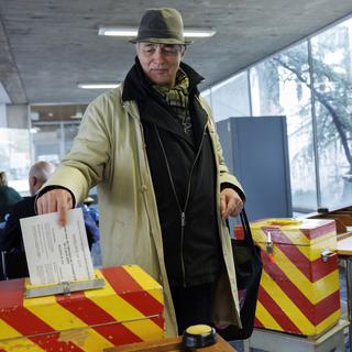 Un citoyen glisse son bulletin de vote dans l'urne aux couleurs genevoises dans le bureau de vote de Carouge (GE). [Keystone - Salvatore Di Nolfi]