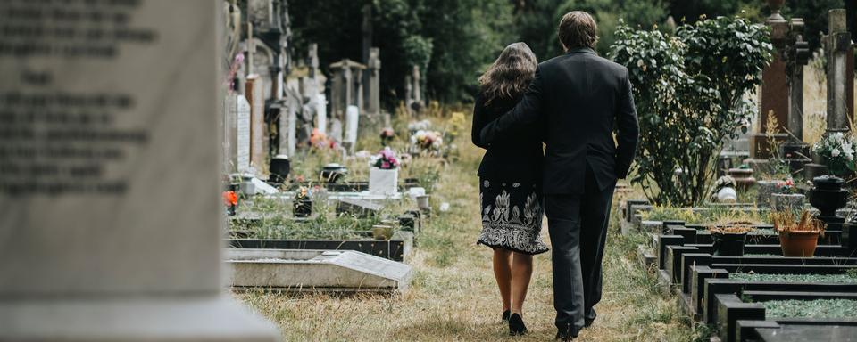 Deux personnes vues de dos marchent dans un cimetière. [Depositphotos - Rawpixel]