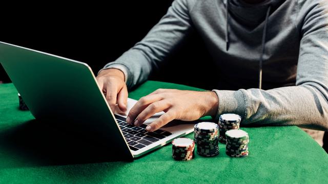 Gros plan sur les mains d'une personne qui joue au poker en ligne. [Depositphotos - VitalikRadko]