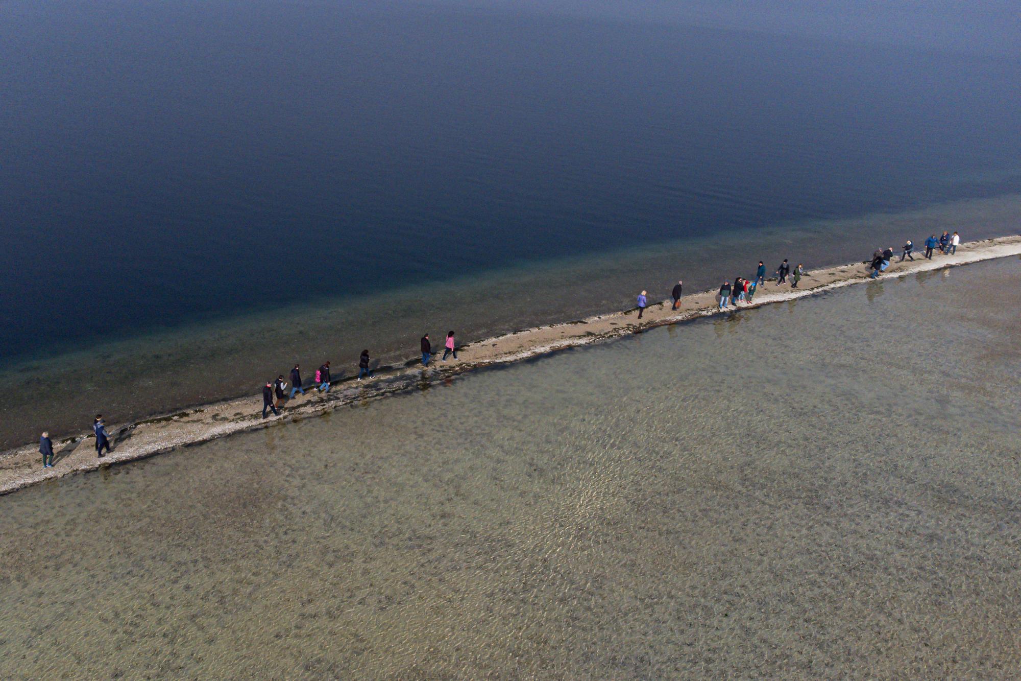 Des visiteurs empruntent un étroit reliant l'îlot de San Biagio à Manerba del Garda, sur le lac de Garde, le 21 février 2023 en Italie. [AFP - PIERO CRUCIATTI]