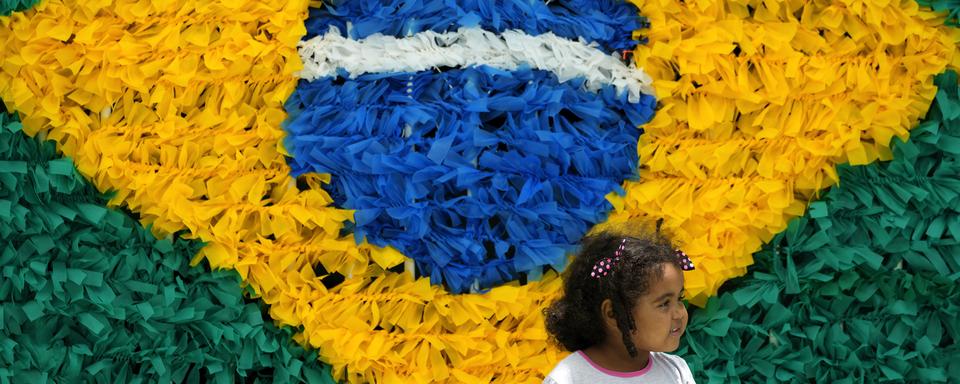 Une petite fille brésilienne en face d'un drapeau de son pays en plastique recyclé (image d'illustration). [Keystone/AP Photo - Eraldo Peres]