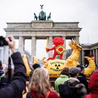 Une action de Greenpeace à Berlin mettant en scène le succès du mouvement écologiste allemand à travers la personnification du soleil antinucléaire triomphant du "dinosaure" de l'énergie atomique. [Keystone/EPA - Clemens Bilan]