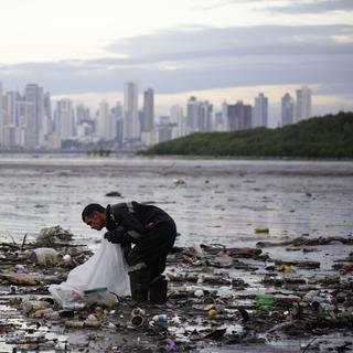 Une personne ramasse des déchets qui flottent dans la baie de Panama City, au Panama (image d'illustration). [Keystone/EPA - Carlos Lemos]
