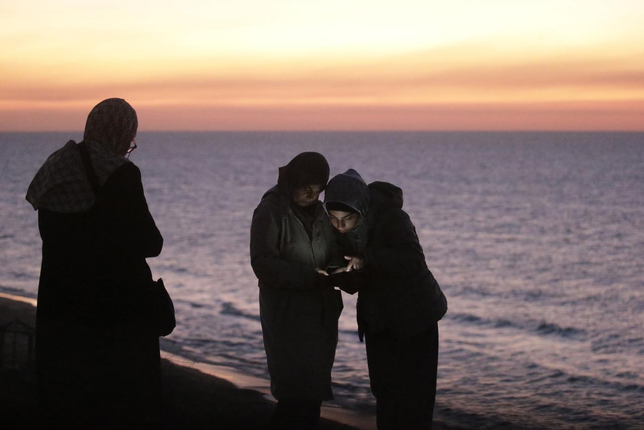 Des Palestiniennes cherchent du réseau sur une plage de Gaza. [Keystone - EPA/Mohamemd Saber]