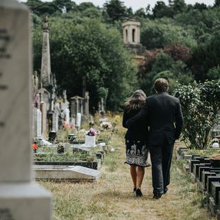 Deux personnes vues de dos marchent dans un cimetière. [Depositphotos - Rawpixel]