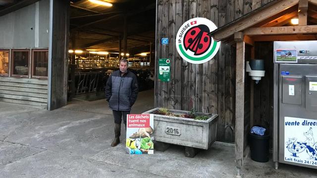 Un agriculteur de La Tour-de-Trême (FR) à coté de l'affiche de la nouvelle campagne de l'Union suisse des Paysans (USP). [RTS - Camille Degott]