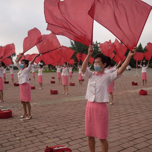 Des membres du Comité du district central de la ville de Pyongyang de l'Union des femmes socialistes de Corée exécutent une routine de propagande en agitant un drapeau aux heures de pointe, sur la place du Grand Théâtre, le 19 juin 2021. [AFP - KIM WON JIN]