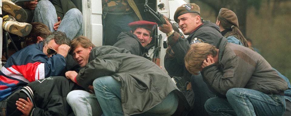 Un soldat des forces spéciales bosniaques riposte, le 6 avril 1992, dans le centre de Sarajevo alors que lui-même et des civils sont pris pour cibles par des tireurs d'élite serbes. Ceux-ci tiraient depuis le toit d'un hôtel sur une manifestation pour la paix réunissant quelque 3'000 personnes, alors que les combats entre combattants bosniaques et serbes s'intensifiaient dans la capitale de la Bosnie-Herzégovine. [Keystone/EPA - Mike Persson]