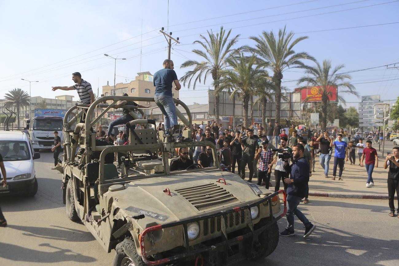 Des Palestiniens montent à bord d'un véhicule militaire israélien pris dans une base de l'armée envahie par des militants du Hamas près de la barrière de la bande de Gaza, dans la ville de Gaza, le samedi 7 octobre 2023. [Keystone - AP Photo/Abed Abu Reash]