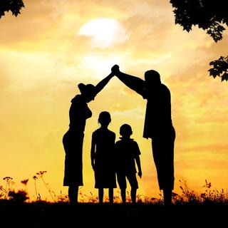 Une silhouette de famille devant un coucher de soleil. [Depositphotos - zurijeta]