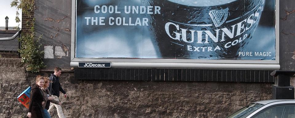 Un groupe de jeunes passe devant une publicité une célèbre bière irlandaise, à Dublin. [Keystone/AP Photo - John Cogill]