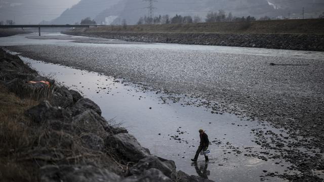 Un homme marche sur le Rhin en pleine sécheresse. [Keystone - Gian Ehrenzeller]