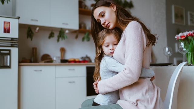 Maman étreint sa fille dans la cuisine, les deux visages ont une expression de tristesse calme ou de tristesse. [Depositphotos - ©Mne_len]