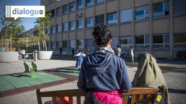 Deux personnes migrantes sur un banc sur un eplace de jeux située à l'extérieur du centre fédéral d'asile à Balerna, au Tessin. [Keystone/Ti-Press - Francesca Agosta]