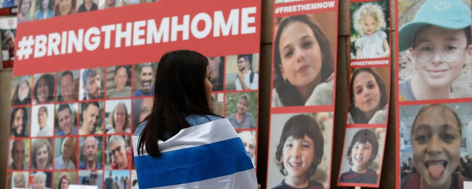 Une jeune femme recouverte du drapeau israélien regarde les portraits des personnes kidnappées par le Hamas. [Keystone/EPA - Robert Ghement]