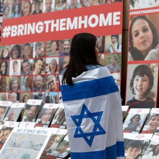 Une jeune femme recouverte du drapeau israélien regarde les portraits des personnes kidnappées par le Hamas. [Keystone/EPA - Robert Ghement]