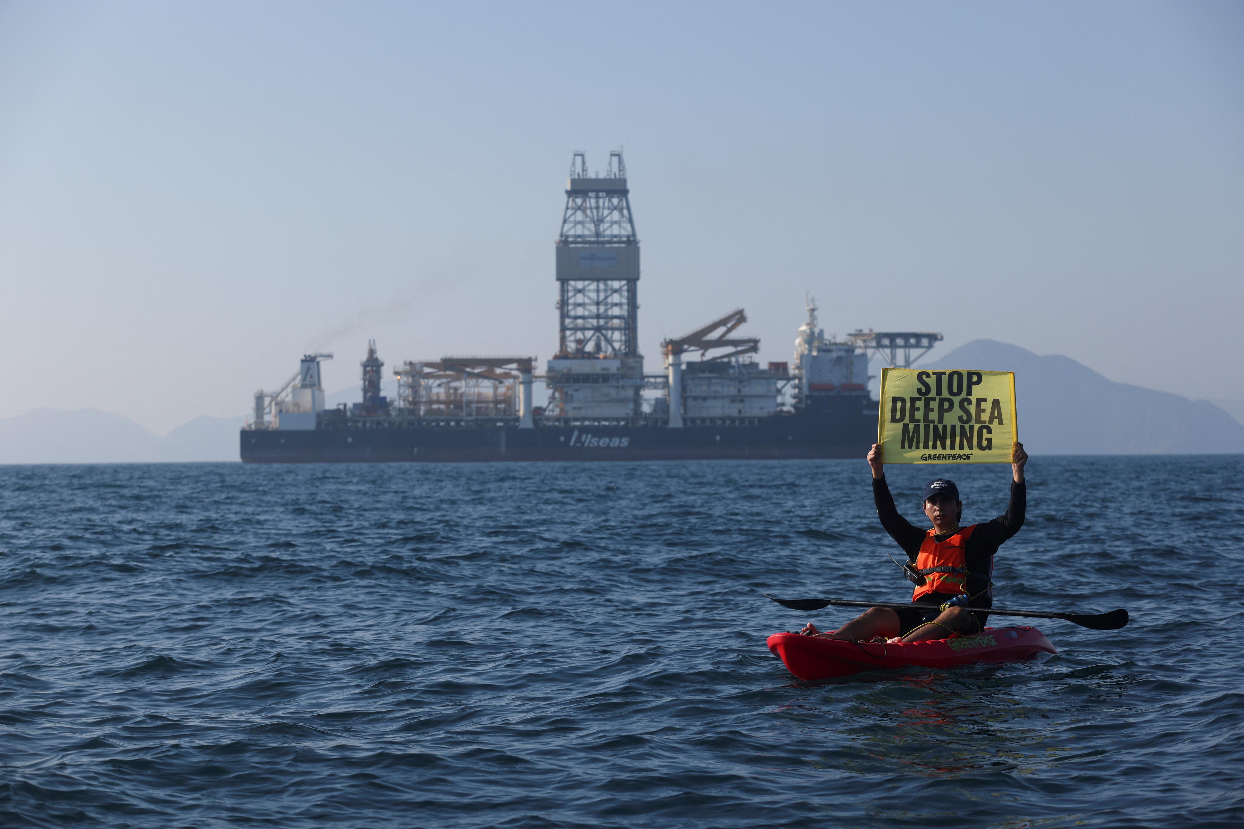 Un militant de Greenpeace brandit une pancarte face au navire d'exploitation minière en eaux profondes Hidden Gem, affrété par l'entreprise canadienne The Metals Company, alors qu'il rentre au port après huit semaines d'exploitation minière expérimentale dans le Pacifique au large du Mexique, le 16 novembre 2022. [Reuters - Gustavo Graf]
