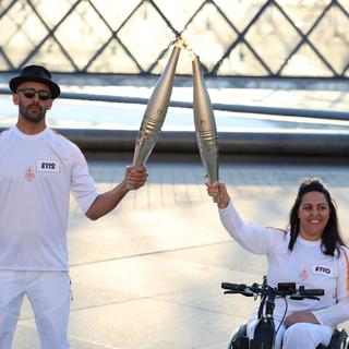 Le relai de flammes olympiques entre l'artiste JR et l'athlète paralympique Sandra Loura. [Keystone/EPA - Julien Mattia]