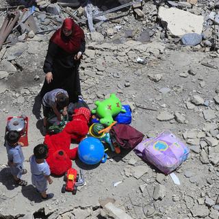 Une femme et ses enfants avec leurs affaires près de jouets récupérés après un tir israélien qui a détruit leur maison dans le village Aita al-Shaab au Liban. [Keystone/AP Photo - Mohammed Zaatari]