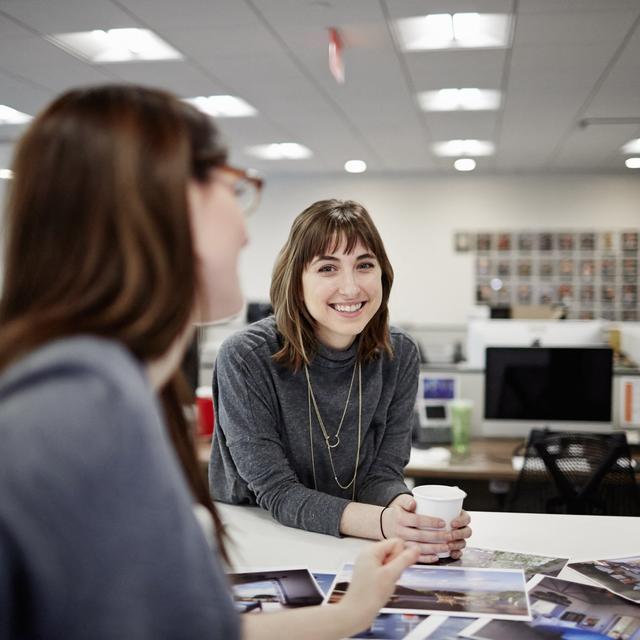 Deux femmes assises dans un bureau discutent et rient. [Mint Images via AFP - Mint Images]