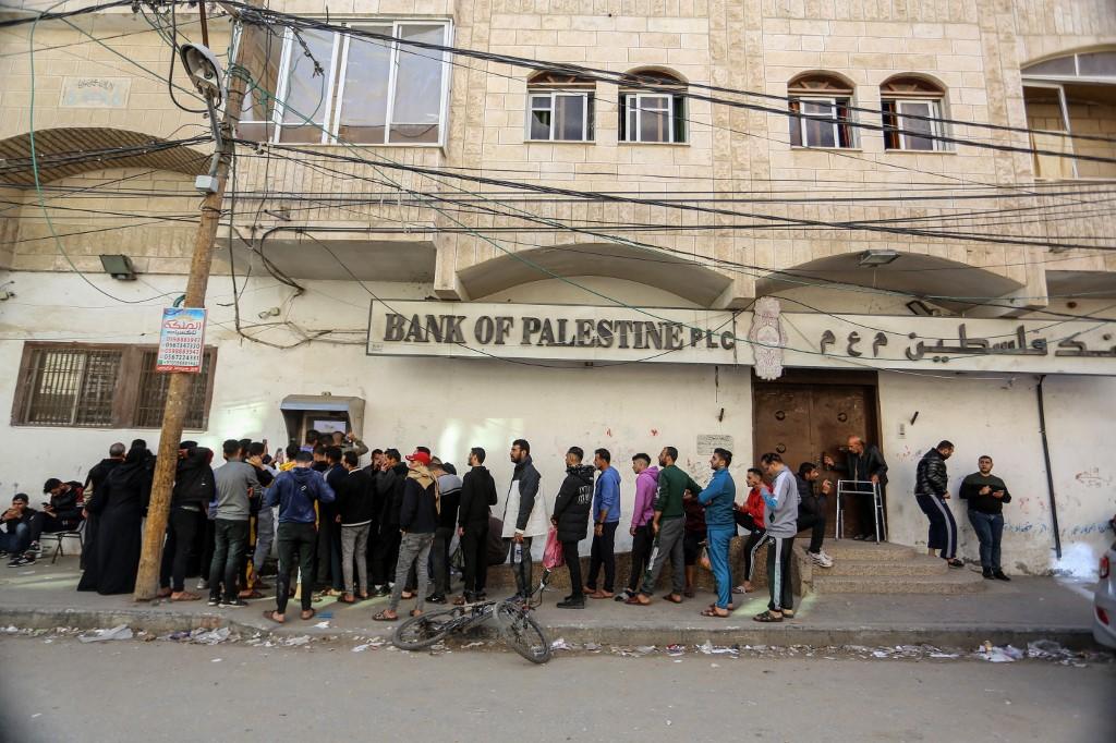 Des Palestiniennes et Palestiniens attendent devant un distributeur de billet de la Banque de Palestine: le gouvernement a déposé les salaires de la population pour une courte période après les attaques du 7 octobre. Gaza City, le 8 décembre 2023. [Anadolu via AFP - Abed Rahim Khatib]