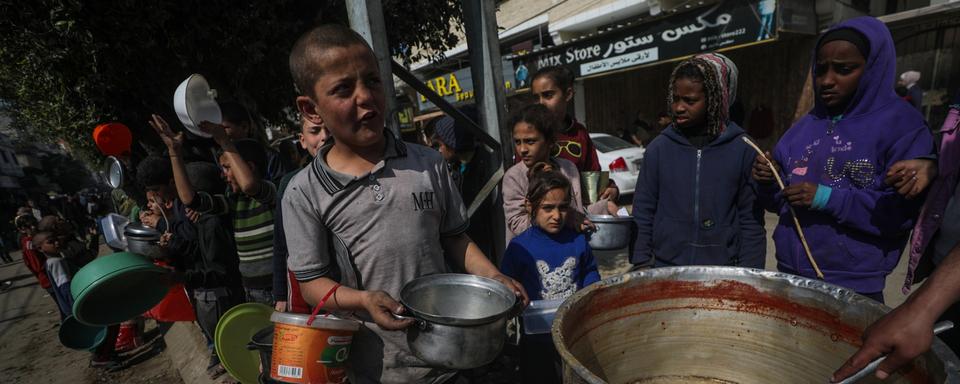 Des enfants palestiniens déplacés font la queue pour recevoir de la nourriture fournie par des donateurs arabes et palestiniens dans la ville de Deir Al Balah, au sud de la bande de Gaza, le 24 février 2024. [Keystone - EPA/MOHAMMED SABER]