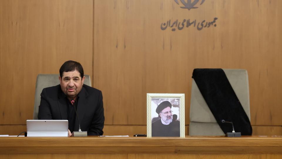 Le président iranien par intérim Mohammad Mokhber pose à côté de la photo de son prédécesseur défunt Ebrahim Raïssi. [KEYSTONE - IRANIAN PRESIDNETIAL OFFICE HAND]