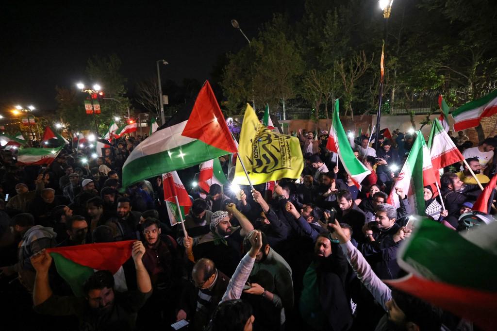 Des manifestants, rassemblés devant l'ambassade britannique à Téhéran, brandissent le drapeau iranien et des drapeaux palestiniens, après que l'Iran a lancé une attaque de drones et de missiles contre Israël. [AFP - ATTA KENARE]