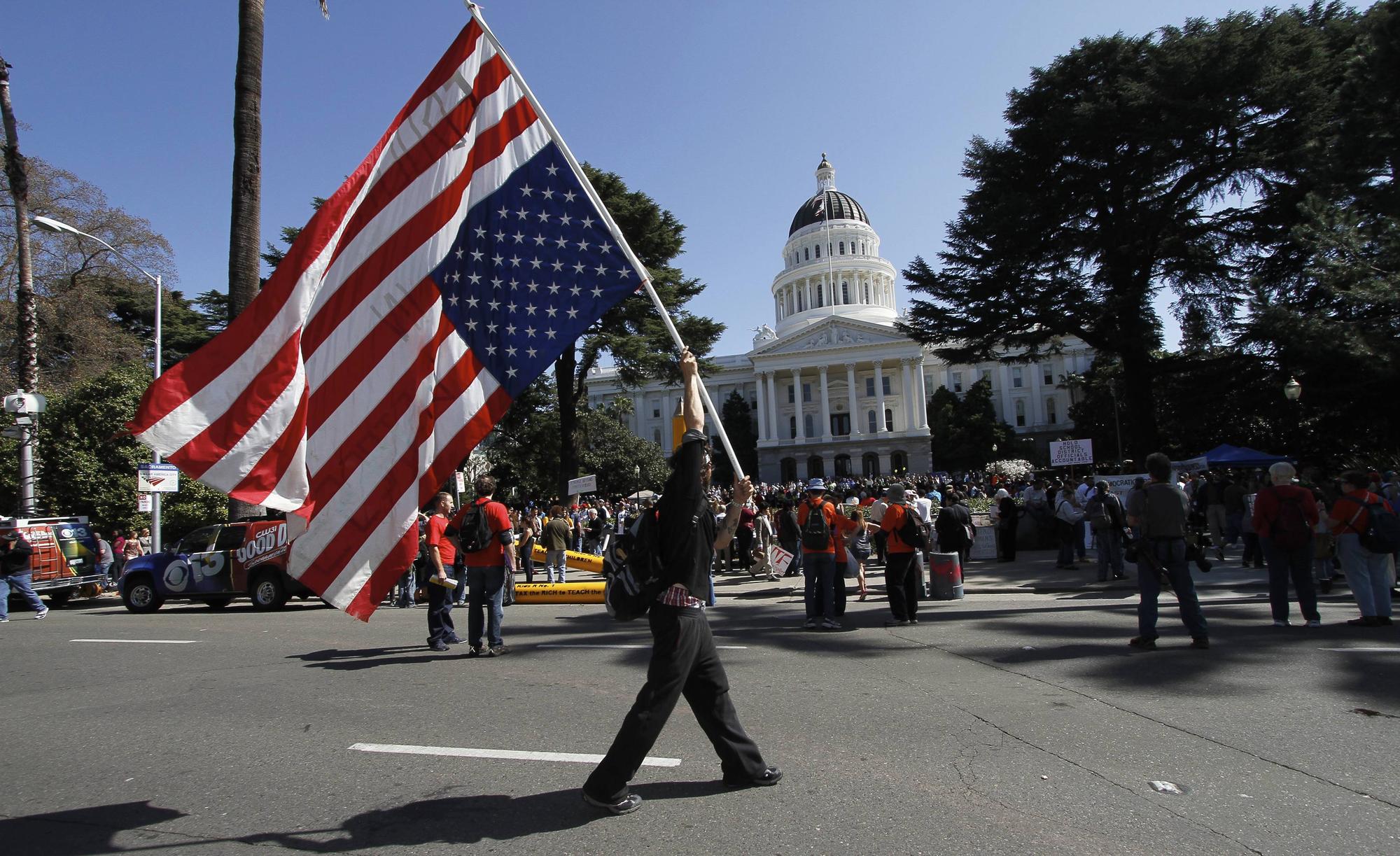 Une personne porte un drapeau américain à l'envers lors d'une manifestation au Capitole de l'État de Californie, à Sacramento. [REUTERS - Kevin Bartram]